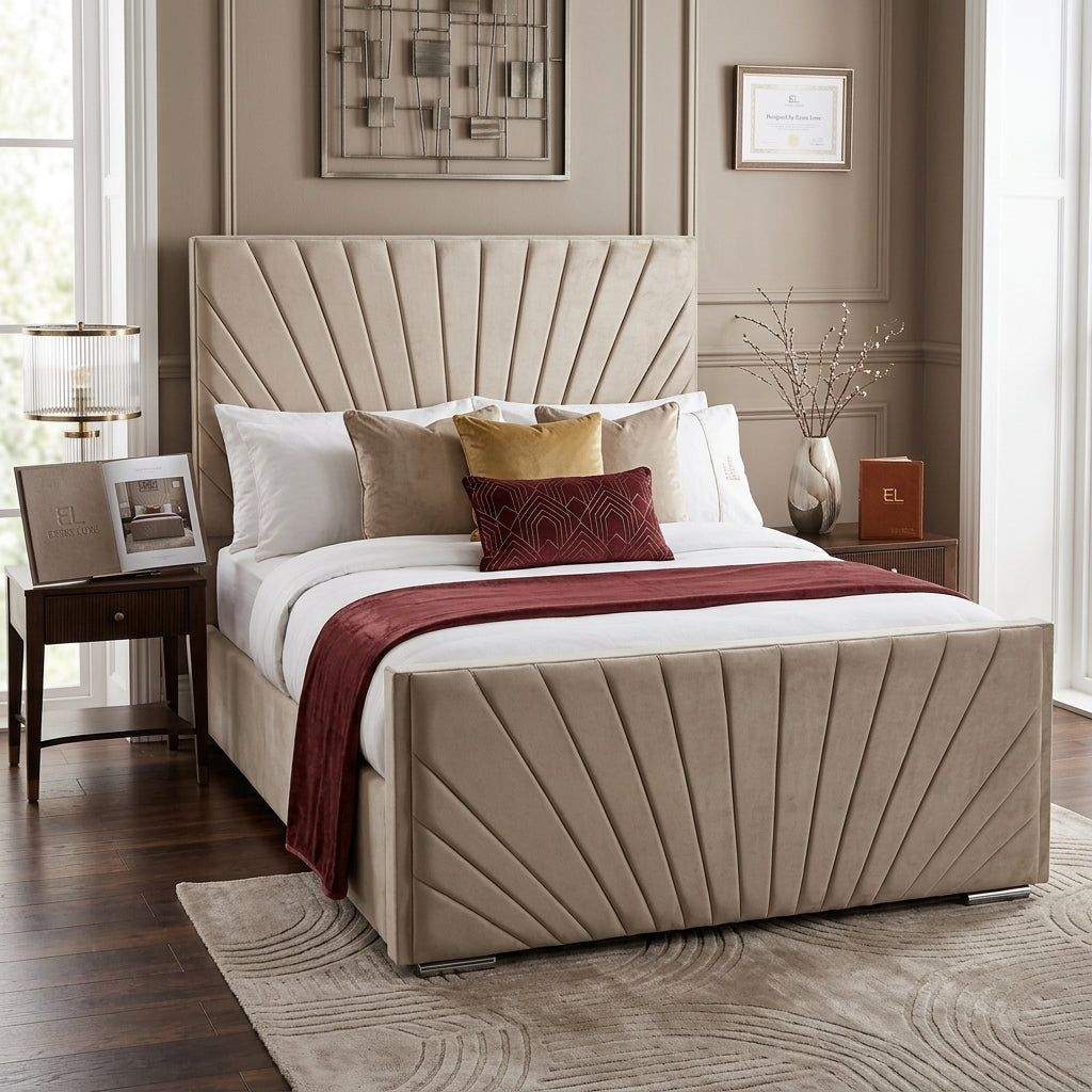 A beige upholstered bed with a tall pleated headboard and matching footboard, styled in a bedroom with white bedding, tan and burgundy accent pillows, a dark wood nightstand, and framed wall art.
