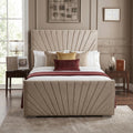 A beige upholstered bed frame with a pleated, sunburst-style headboard and matching footboard, styled in a modern bedroom setting with white bedding, decorative pillows, and side tables.